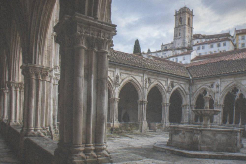 A stone cloister with carved arches and a fountain in a Portuguese monastery