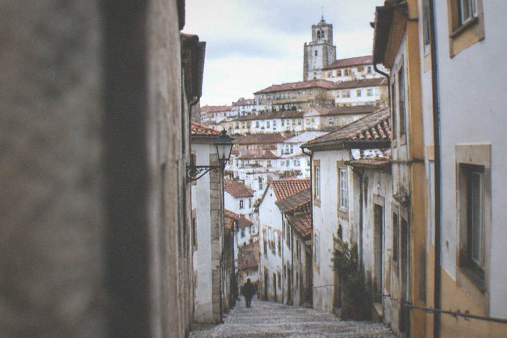 A narrow cobbled street climbing between old stone buildings in a Portuguese hill city