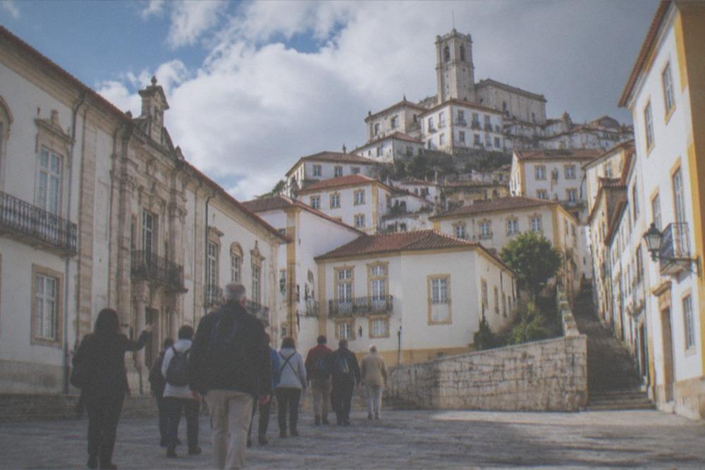 A tour group walking with a guide across a stone square toward a university building