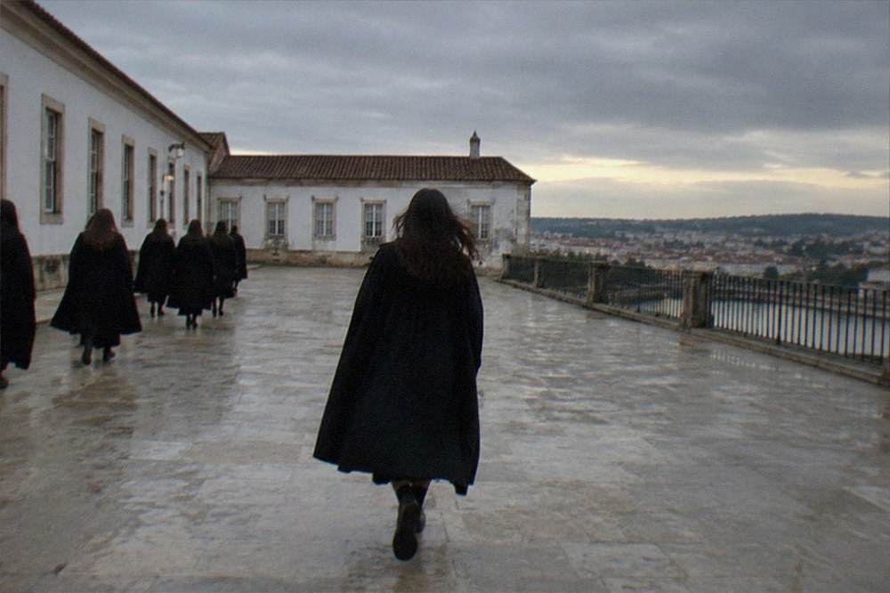 Students in black capes walking through an old university courtyard in the evening
