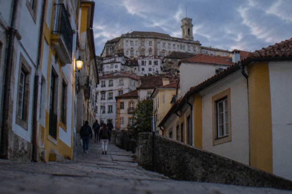 Visitors walking up the stone lane toward the university gates in Coimbra's upper town