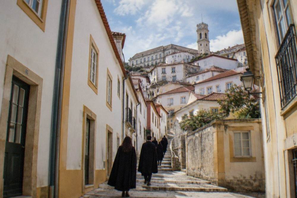 Students in black academic capes walking down a narrow Coimbra street