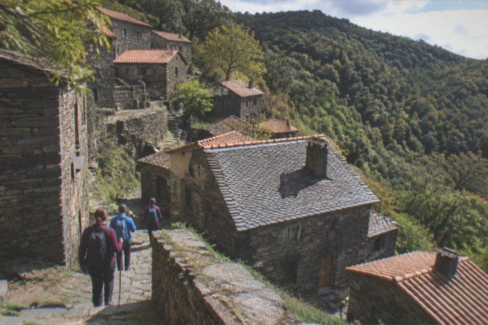 Hikers on a stone path between schist village houses on a forested mountainside