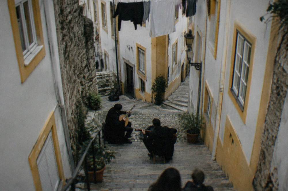 Two musicians in dark student capes performing fado with guitars in a small Coimbra venue