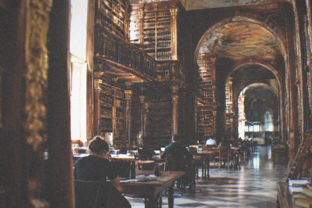 The baroque interior of the Joanina Library with tall wooden bookshelves and a decorated ceiling.