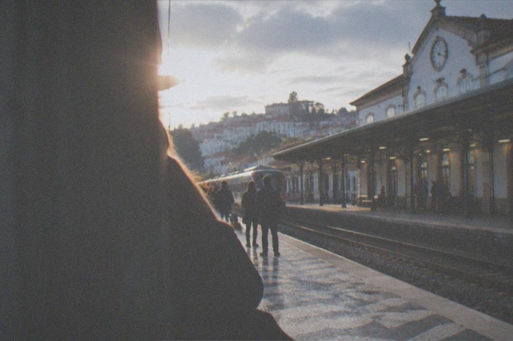 A railway station building in Coimbra with a clock and passengers waiting on the platform.