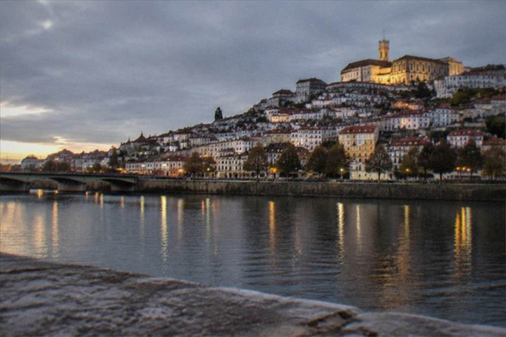 The old town of Coimbra seen from across the River Mondego at night with the university lit above