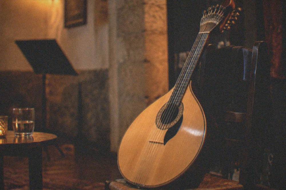 A close view of a Portuguese guitar resting against a chair in a dimly lit performance room