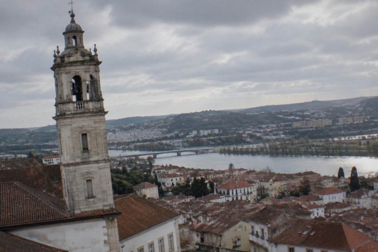 View over the rooftops of Coimbra, Portugal, with the university tower rising above the old town and the River Mondego beyond.