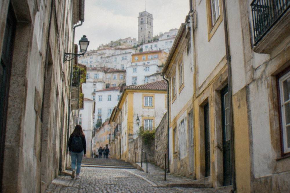 Narrow cobbled street in the old town of Coimbra lined with stone buildings and a student mural.