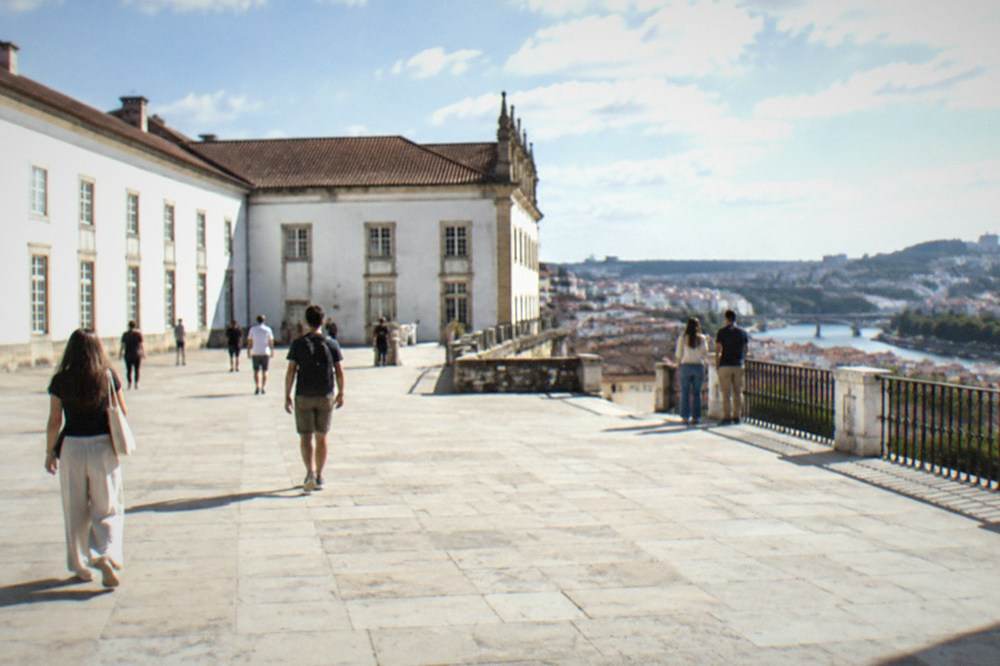 The grand courtyard of the University of Coimbra with visitors walking across the stone paving.