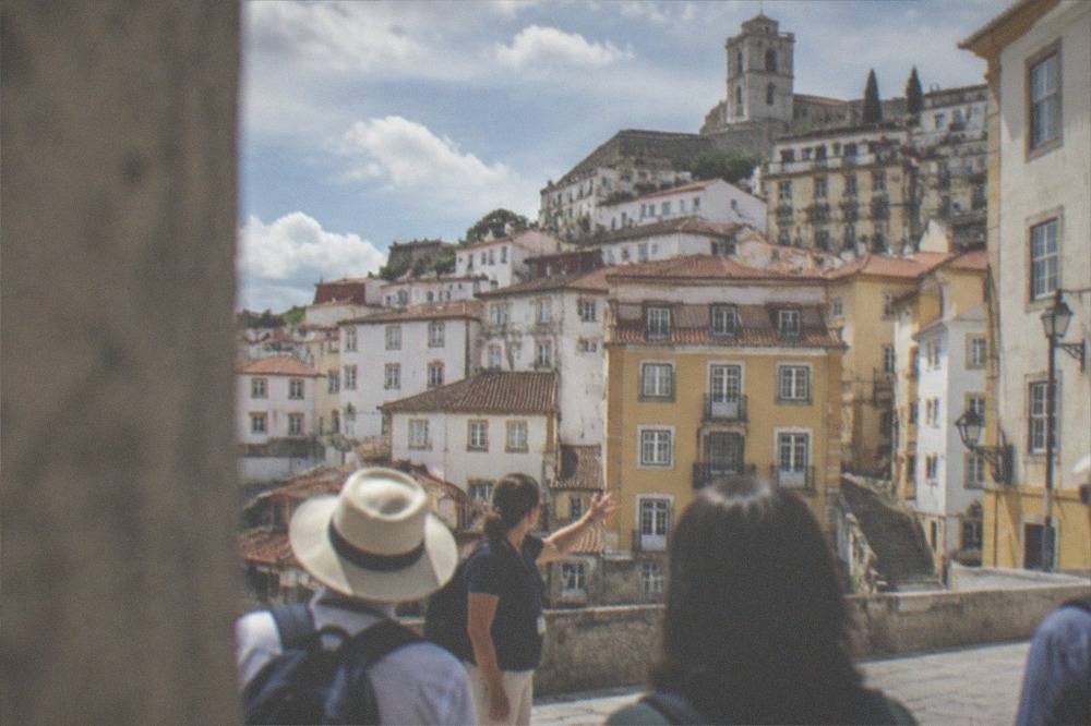 A tour guide speaking to a small group of visitors on a stone square in Coimbra's old town.