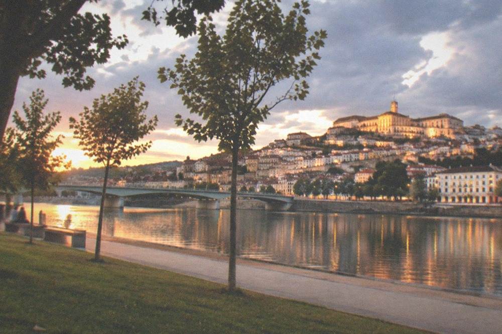 The River Mondego at dusk with the illuminated old town of Coimbra reflected in the water.