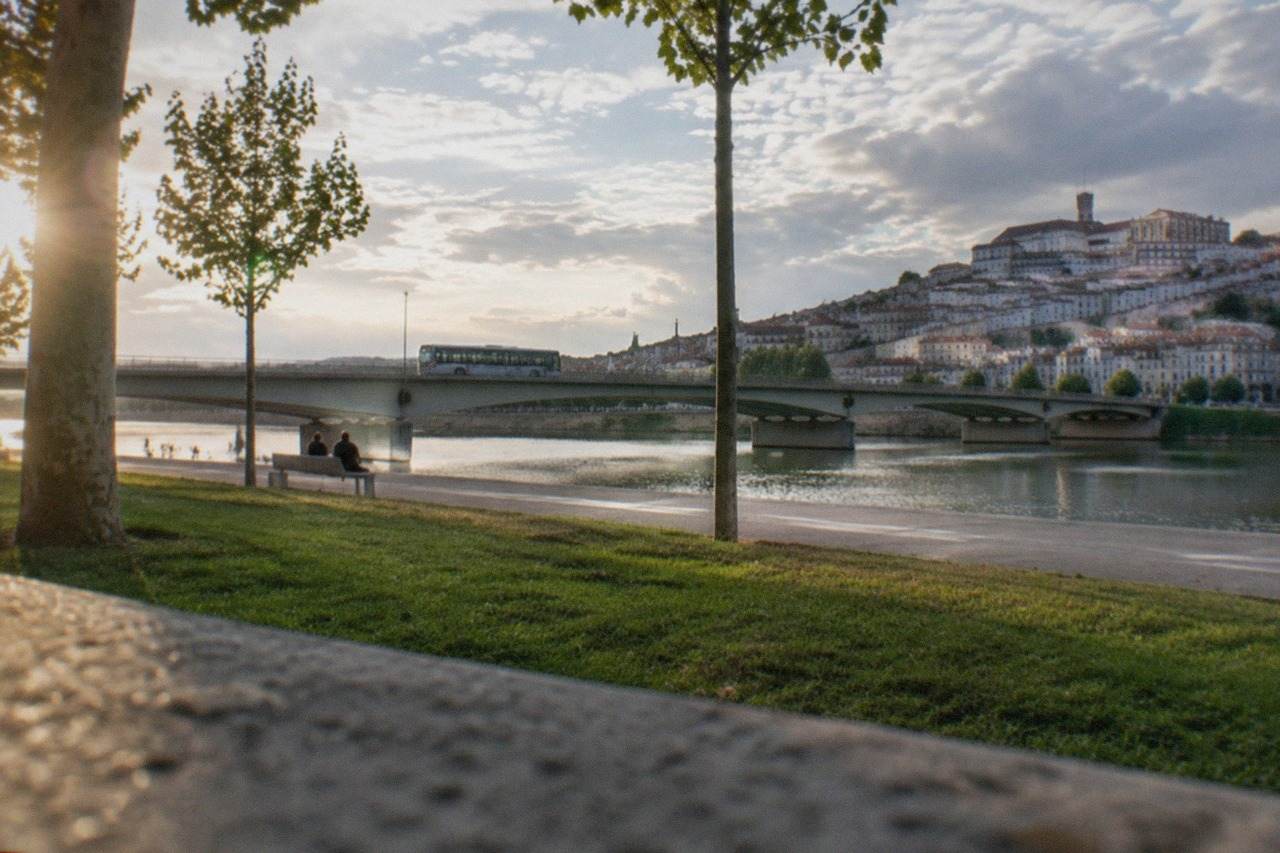 A city bus crossing a bridge over the River Mondego with Coimbra's old town rising on the far bank