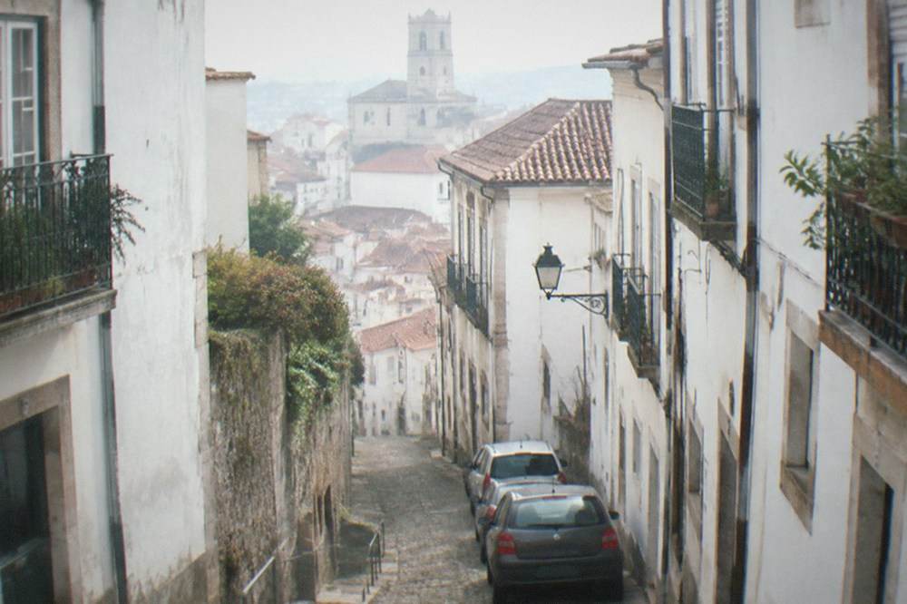 A narrow lane in Coimbra's upper town with parked cars barely fitting between old stone walls