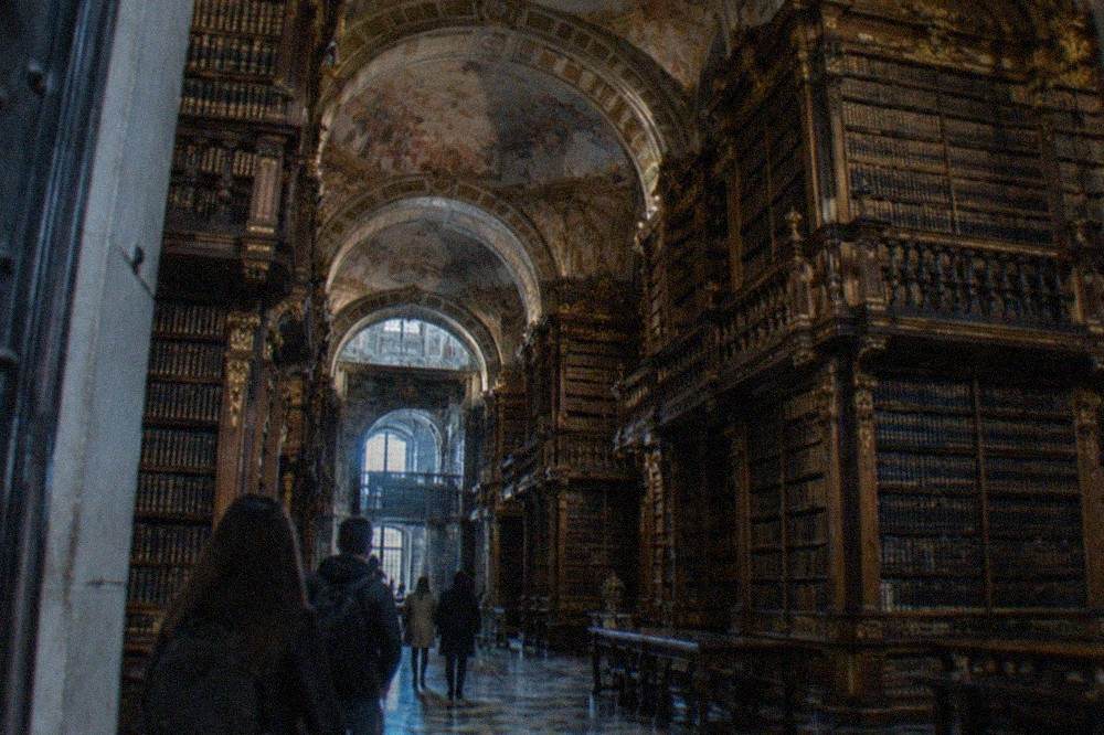Visitors entering the baroque Biblioteca Joanina through its stone doorway on a timed slot