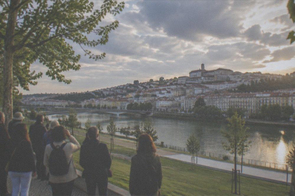 A tour group pausing on the university hill overlooking the River Mondego in soft evening light