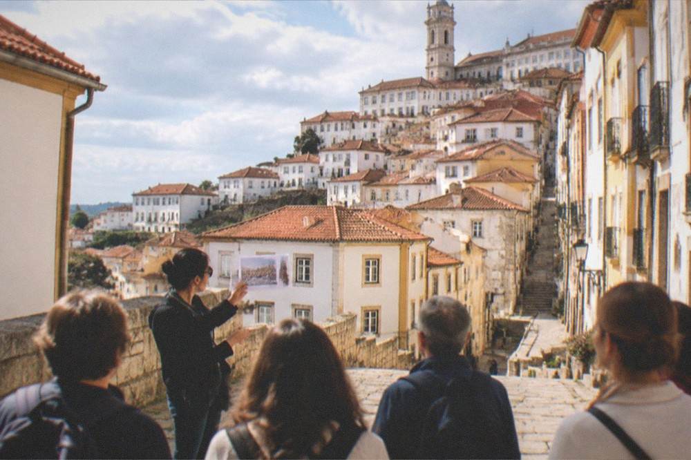 A guide holding up a printed ticket while explaining the visiting route to a tour group in Coimbra