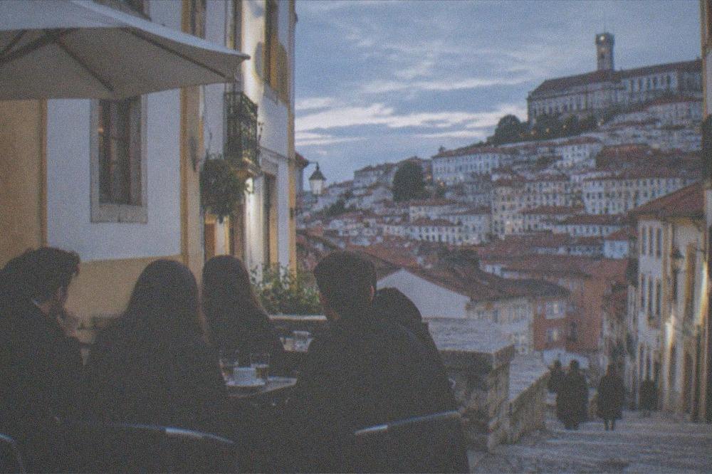Coimbra students in black academic capes gathered around a café table