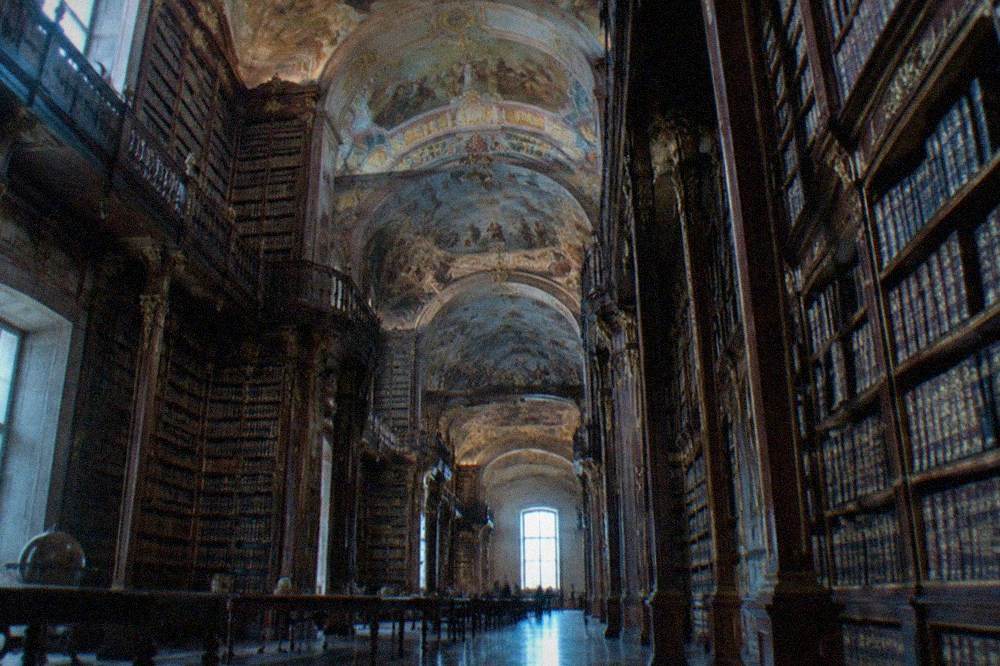 The ornate baroque interior of the Biblioteca Joanina with tall wooden bookshelves and painted ceilings