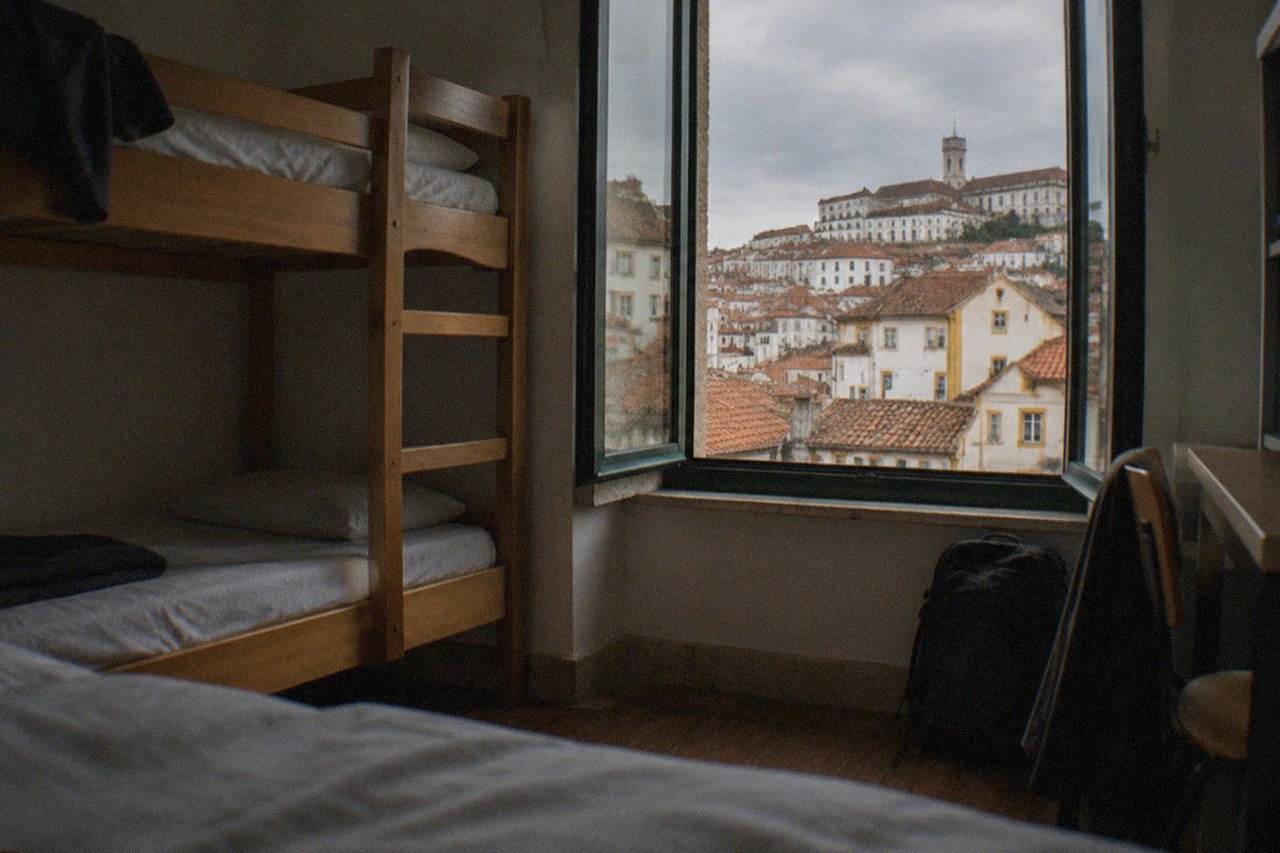 Hostel dorm room with bunk beds and a window overlooking the tiled roofs of Coimbra