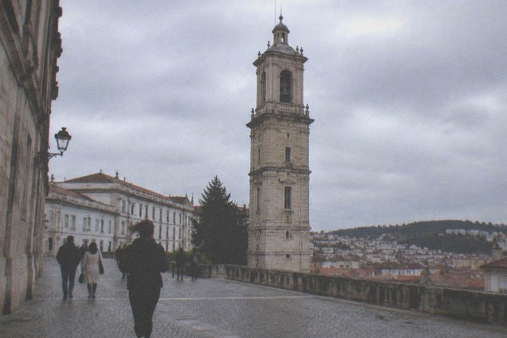 Walkers on a cobbled square in Coimbra old town with the university tower above
