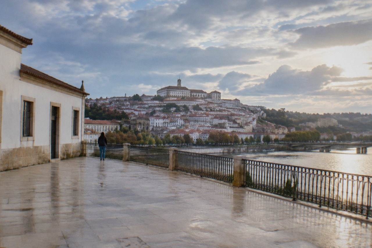 The historic University of Coimbra buildings seen from across the River Mondego on a bright day