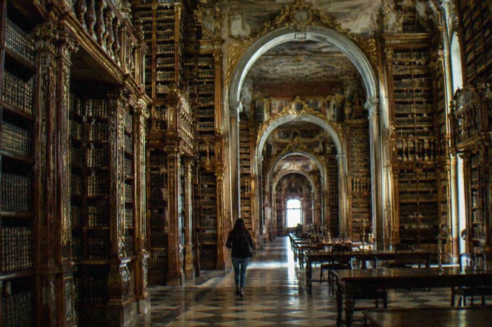 The gilded baroque interior of the Biblioteca Joanina with tall wooden bookshelves