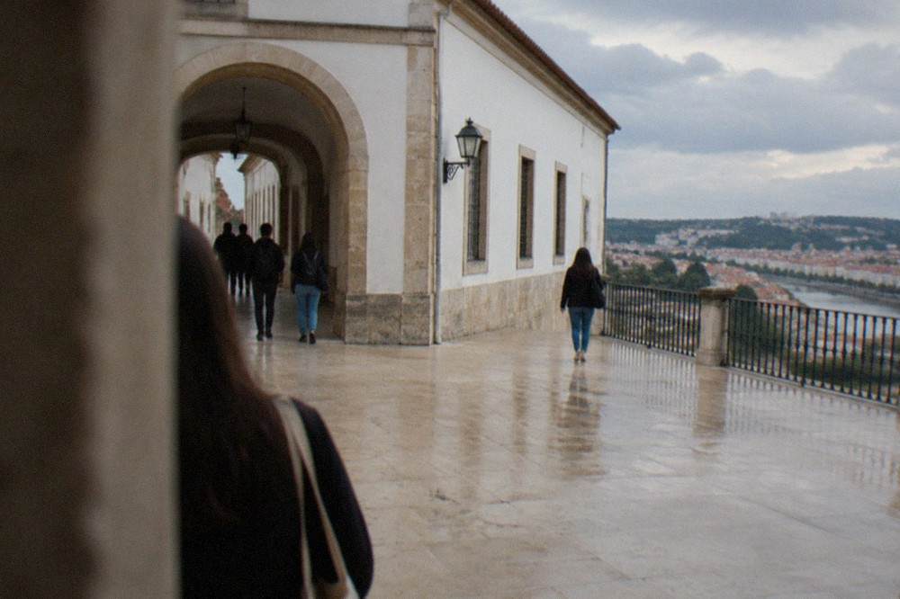 Students and visitors walking through the stone archway courtyard of the University of Coimbra