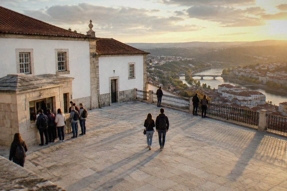 Visitors waiting at a stone ticket kiosk outside the University of Coimbra buildings