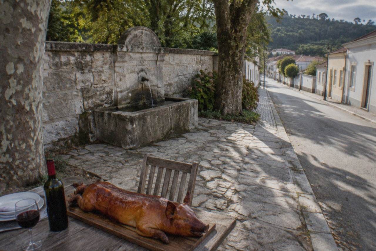 A whole roast suckling pig on a wooden board beside a bottle of red wine