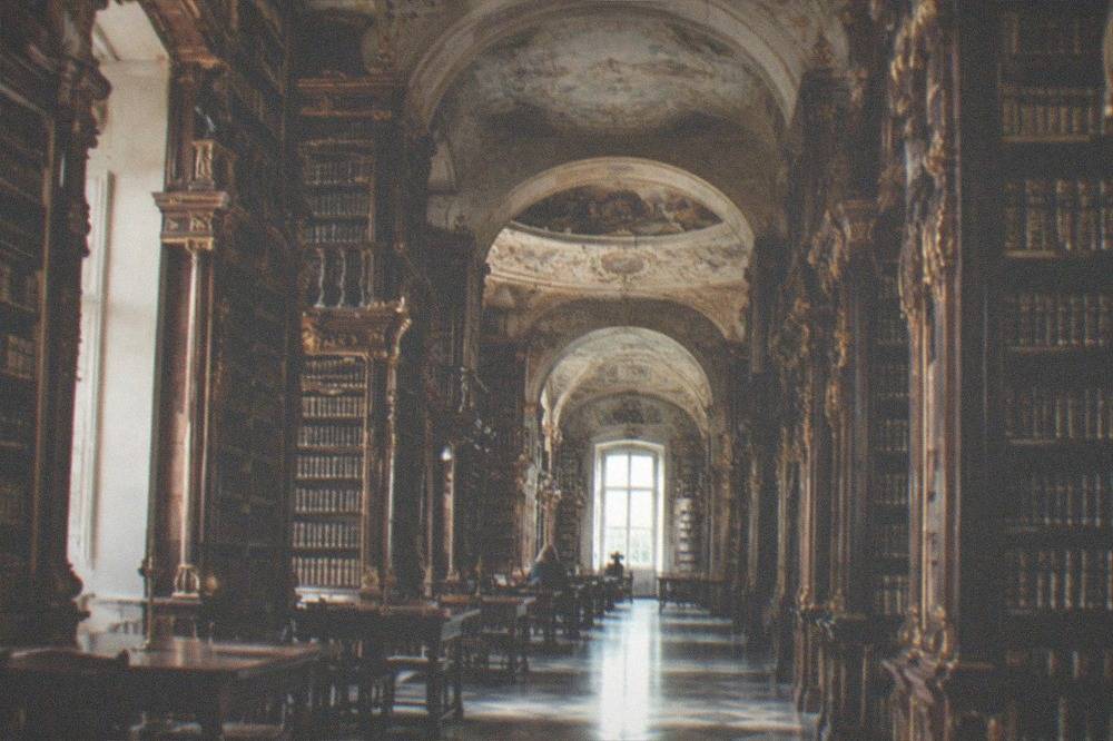 A baroque library hall with tall wooden bookshelves and ornate ceilings