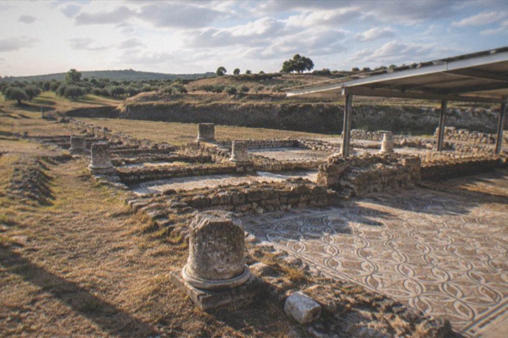 Stone Roman ruins with column bases and mosaic floors under an open sky