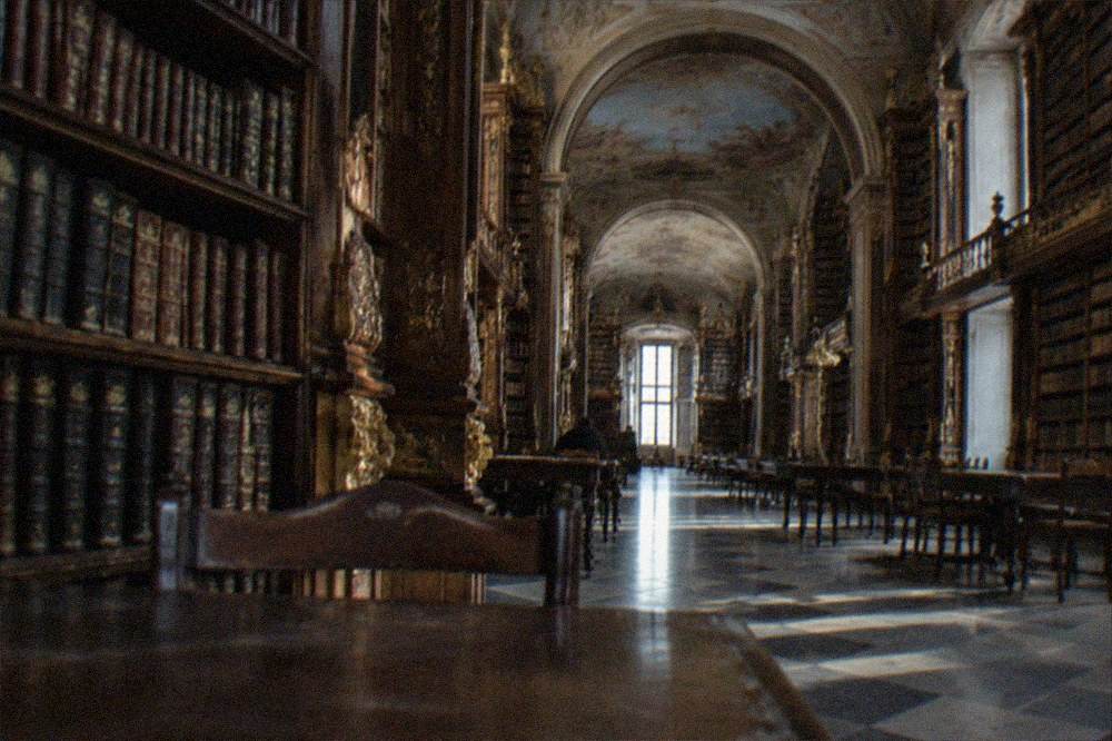A baroque library hall with tall wooden bookshelves and painted ceilings