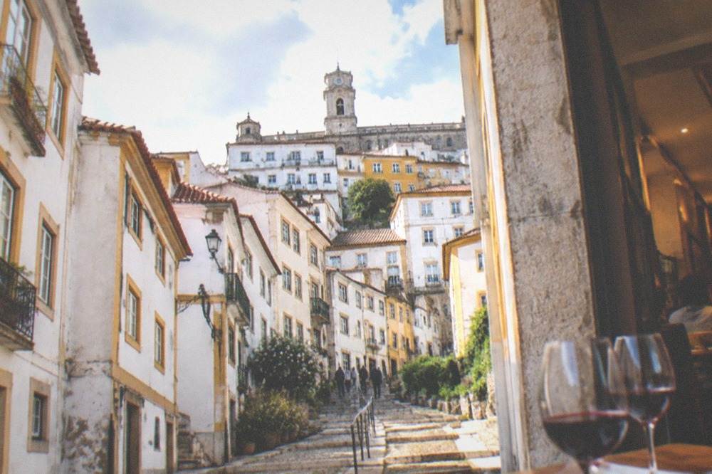 A table with glasses of red wine and small plates inside a busy Coimbra restaurant in the evening
