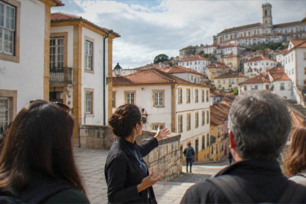 A guide addressing a small group of visitors on an evening walking tour in a Coimbra square