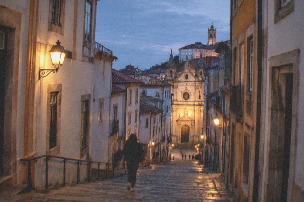 A lit city street in Coimbra at night with the illuminated facade of a church at the end of the block