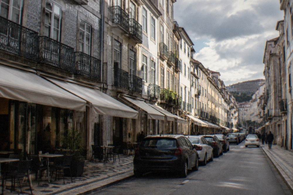 Rows of parked cars along a flat street in Coimbra's lower town with café awnings above the pavement