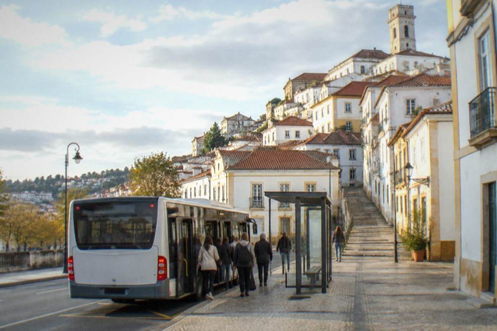 A city bus stopped at a marked bus stop in central Coimbra with passengers boarding
