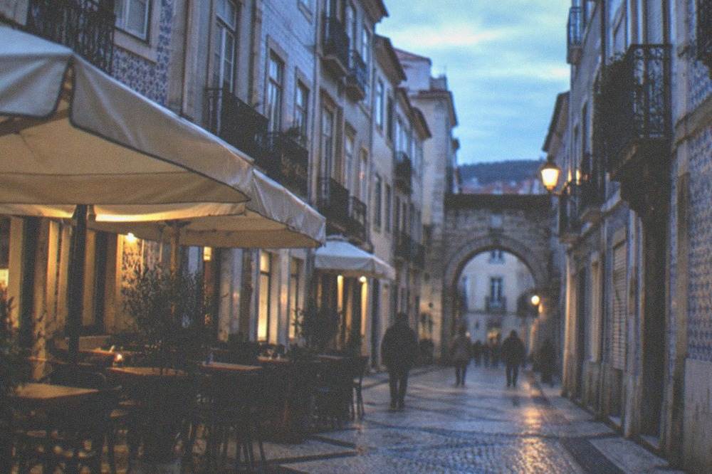 A cobbled street in a Portuguese old town with café awnings and a stone archway