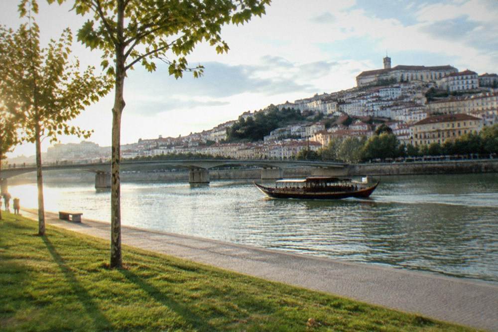 A traditional boat on the River Mondego with the old city of Coimbra rising on the far bank