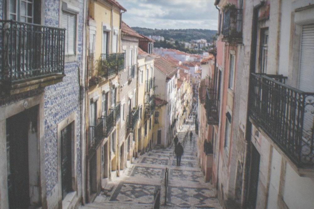 A steep tiled lane in the Baixa of Coimbra with painted facades, iron balconies and worn stone steps