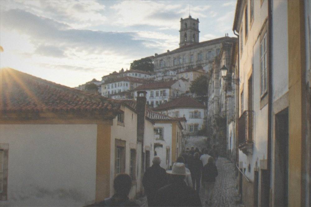 A tour group walking up a narrow cobbled street toward a university building in Coimbra