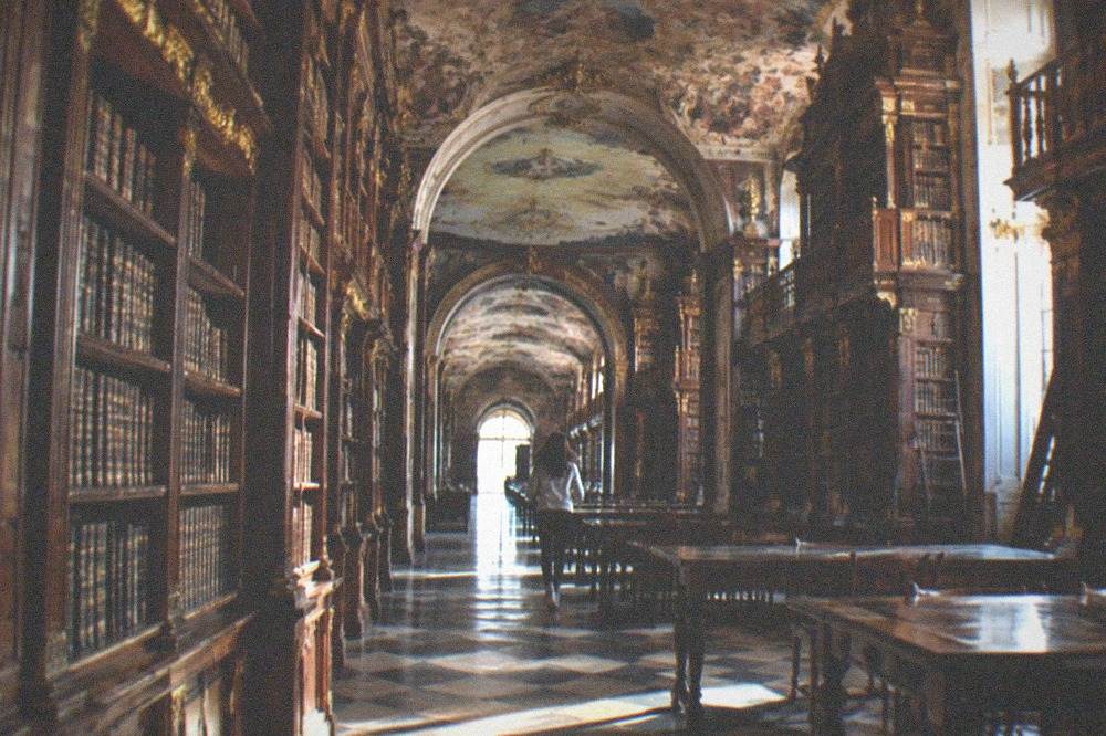 The baroque interior of the Joanina Library with tall wooden bookshelves and painted ceilings