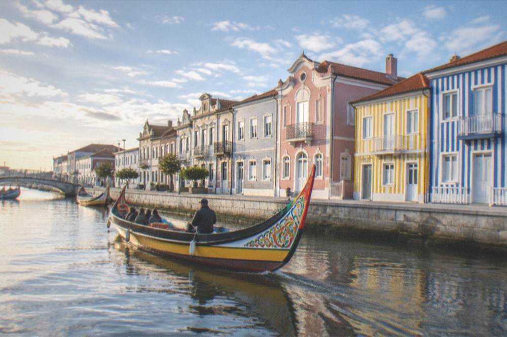 A traditional moliceiro boat gliding along a canal beside coloured striped houses in Aveiro