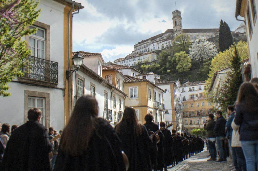 A student parade moving down a Coimbra street lined with spectators