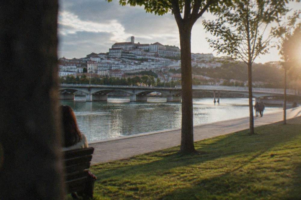 A stone bridge over the River Mondego with the old town of Coimbra rising on the far bank