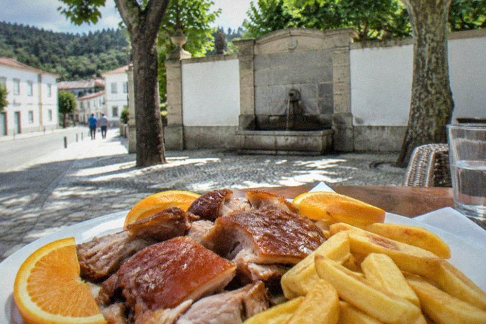 Sliced roast suckling pig with crispy skin served with orange slices and fried potatoes