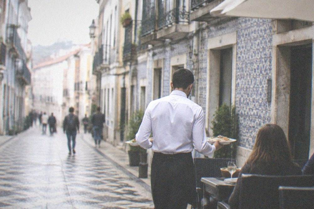 A waiter carrying plates of food to a table outside a small tavern in downtown Coimbra