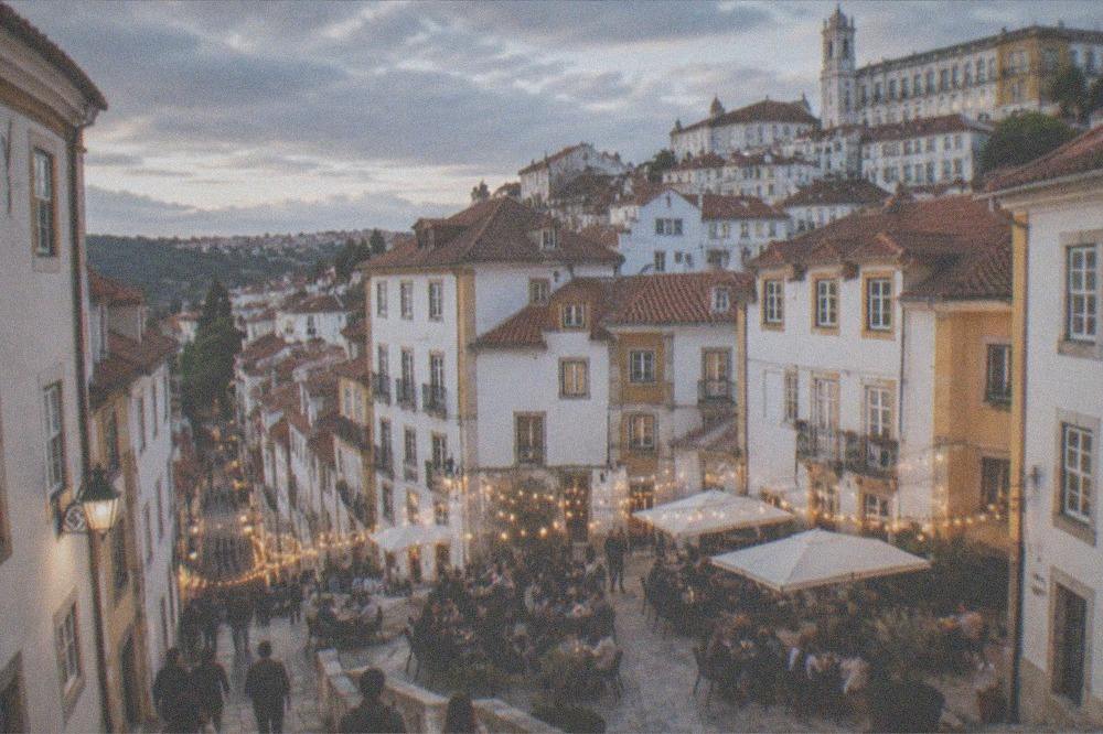 A busy evening square in Coimbra with people gathered around outdoor tables under string lights